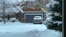Snow falling on a house with a car in the driveway