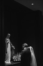 bride and groom praying before a statue of Mary 