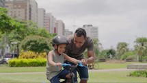 Father's Day. Father teaches son to ride bicycle wearing safety helmet. child learn to ride bicycle in park. Happy family concept and dream. Active father teaches child to ride bike in park
