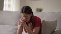 Religious adult woman praying, hands clenched at home
