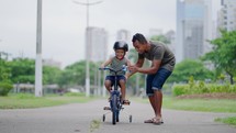happy spending quality time together outdoors with his son. Kid riding bike having fun with his father
