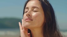 Close-up woman on bikini takes sunscreen of tube, moisturizing lotion applies sunblock on her face