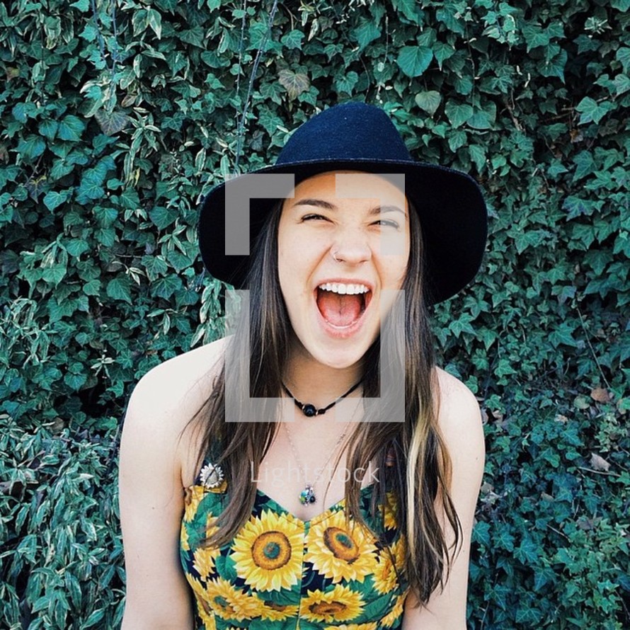 A laughing girl standing against a wall of ivy.