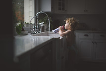 toddler drinking water by a sink 