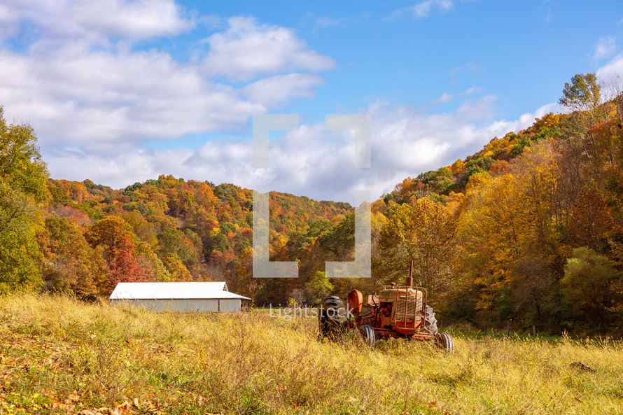 Tractor and barn in grassy field surrounded by trees with autumn fall foliage