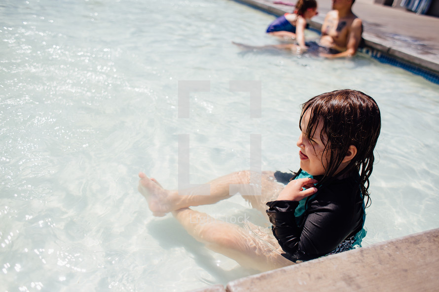 a little girl sitting in shallow pool water 