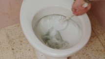 Man's hand with brush cleaning a dirty toilet