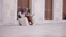 Three young pretty muslim teenagers woman in head scarf chatting and using smartphones
