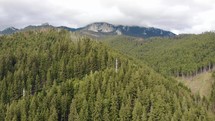 Aerial shot of flying over forested mountains with clouds in the background.