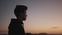 young man standing near the ocean at dusk deep in thought 