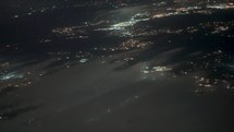 Aerial view of city lights at night through wispy clouds