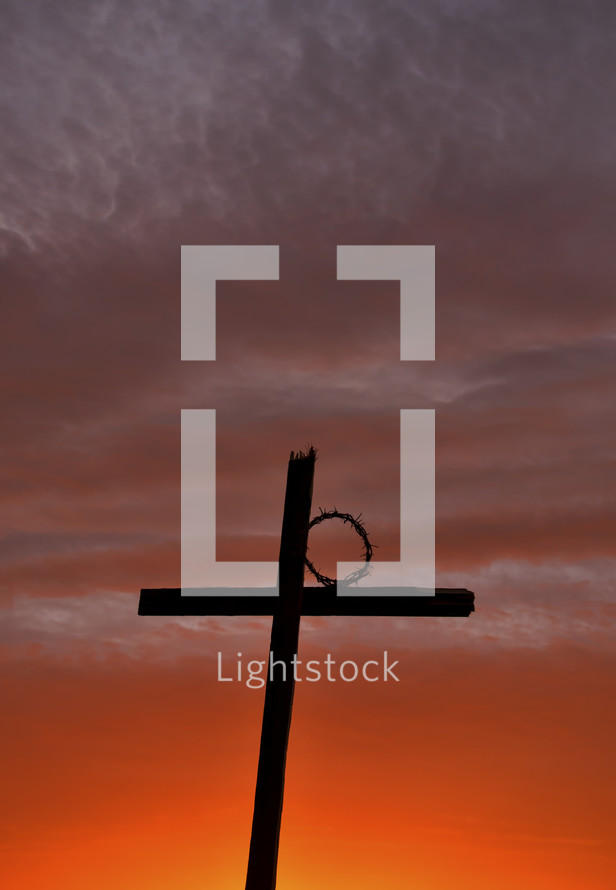 silhouette of a cross and a crow of thorns against a fiery sky at sunset 