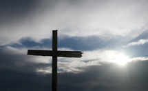 Cross against cloudy sky with sun filtering through