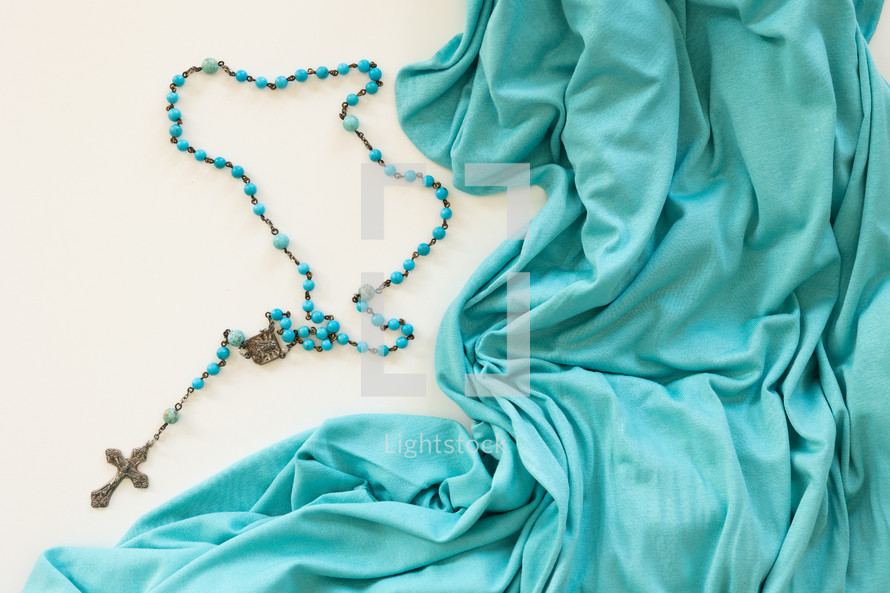 Blue rosary on a white background with teal fabric border