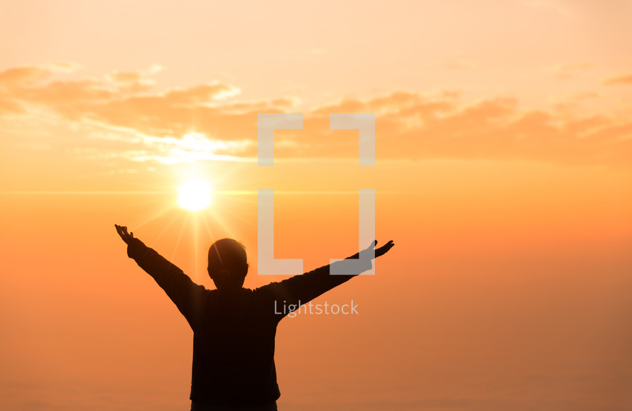 Man's hands raised in worship at sunset