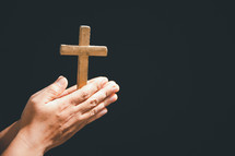 Hands folded on a wooden cross