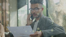 Young entrepreneur sitting in the cafe, analyzing business plan on paper and speaking on mobile phone with partner
