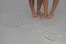 Bare feet by the waters edge with message of love written in the sand