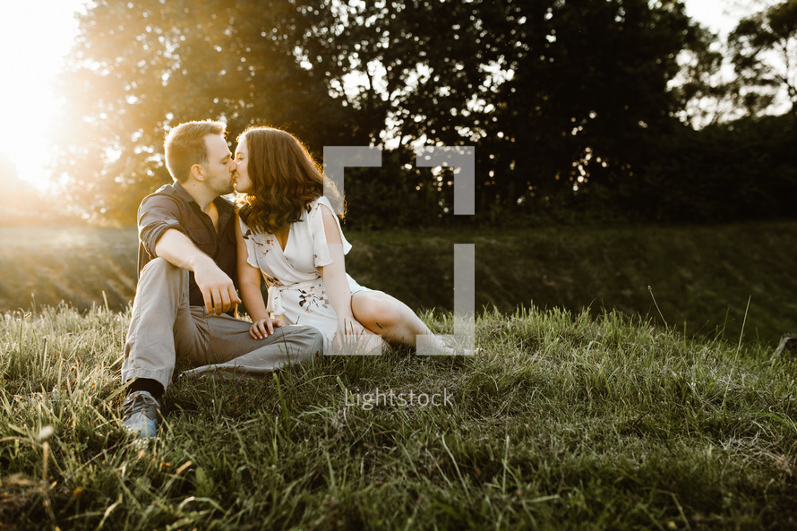 a couple sitting in the grass kissing 