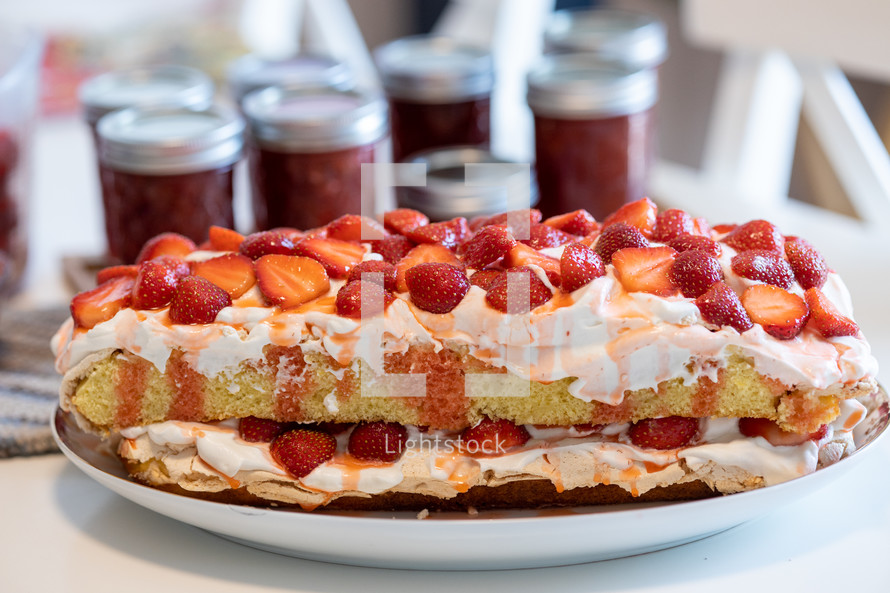 strawberry layer cake in foreground; jars of strawberry jam in background