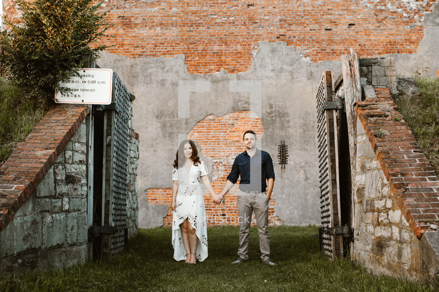 a couple holding hands standing in front of a brick wall 