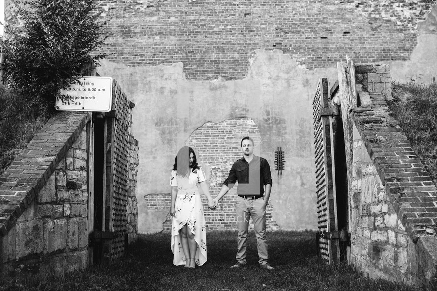 a couple holding hands standing in front of an old brick wall 