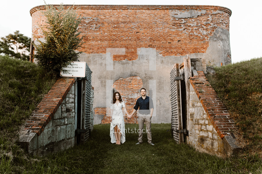 a couple standing in front of a brick building holding hands 