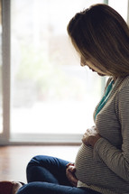 a pregnant woman sitting on the floor praying holding her belly 