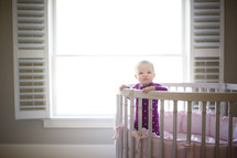 an infant standing in a crib in a nursery 