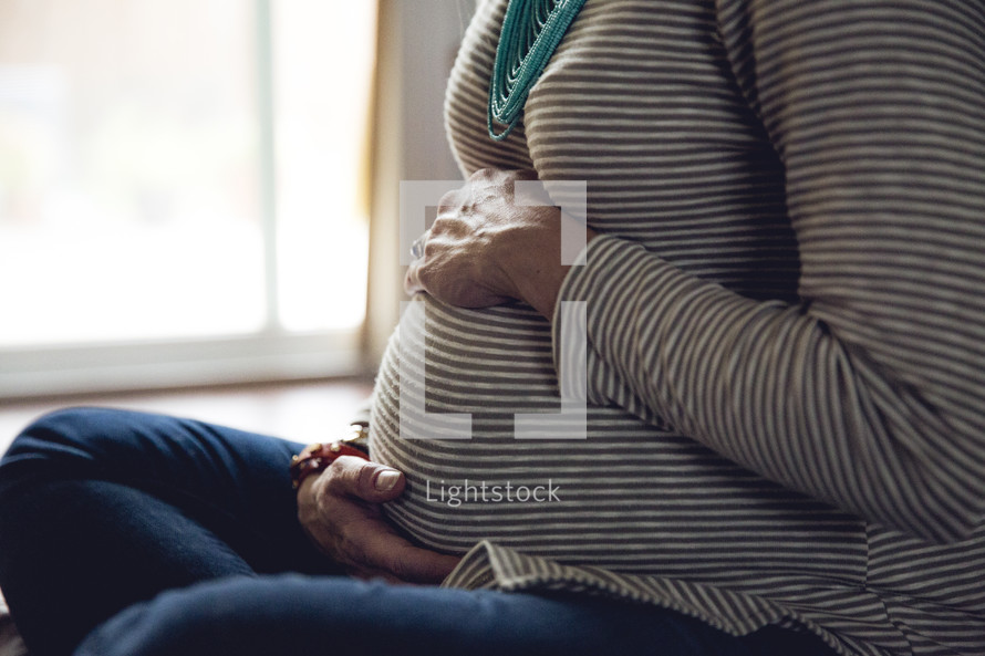 a pregnant woman sitting on the floor praying holding her belly