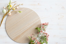 Round wood board with easter eggs and pink flowers on a white wood background