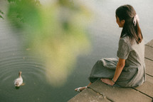 young woman sitting on a bridge feeding ducks 