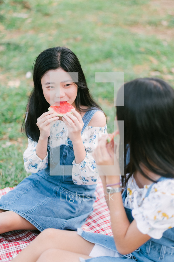 girls eating watermelon on a picnic blanket 