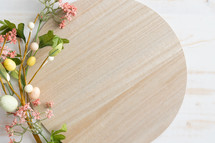 Round wood board with Easter eggs and pink flowers on a white wood background