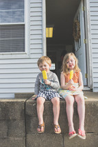 children sitting on a back porch stoop eating popsicles 