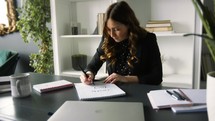a young Caucasian business woman practicing calligraphy in a home office 