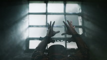 Prisoner with chained hands pray to the Lord. View trough prison window.