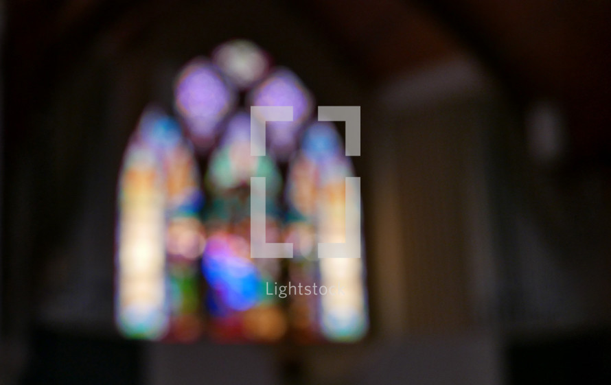 arched stained glass window in church sanctuary with blur effect