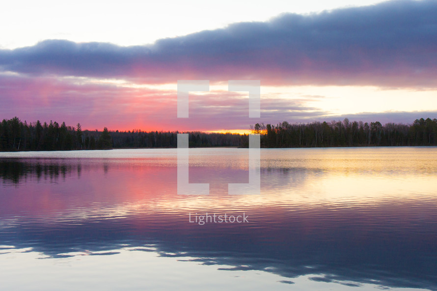 Cloudy pink sunset and evergreen trees on Wolf Lake in Michigan 