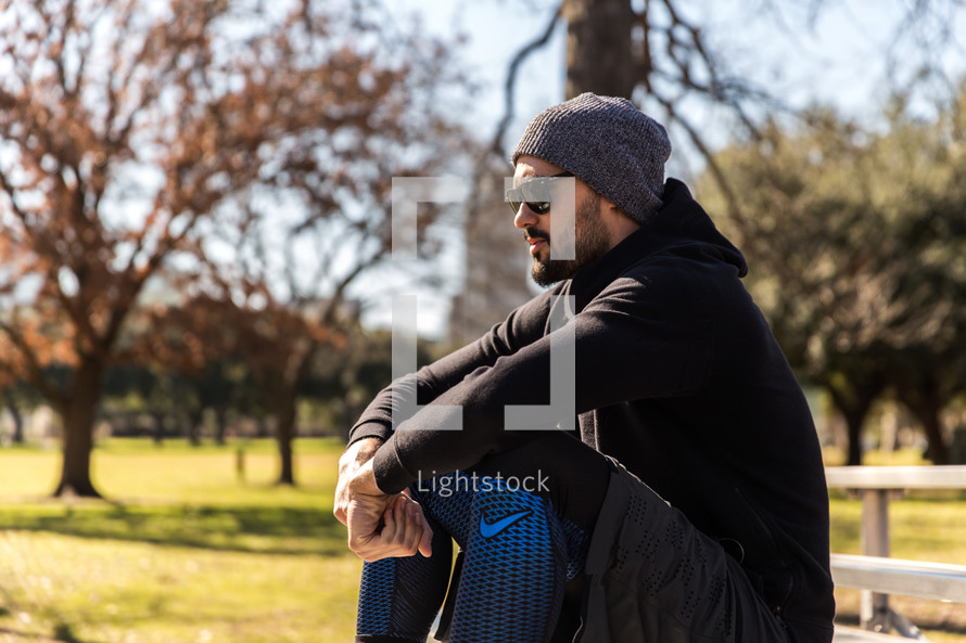 A man wearing workout clothes sits and rests in a park.