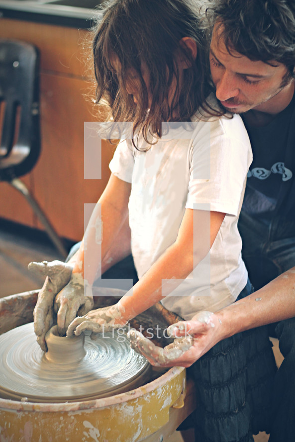 A father helping his daughter create a bowl on the potters wheel.