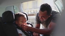 Loving father puts his little cute male child in back seat and makes him smile being playful
