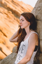 young woman leaning against a rock with closed eyes 