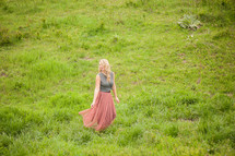 a woman in a long dress standing in tall grass 