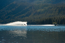 A man water skiing pulled by motorboat on like in California near tree covered slopes