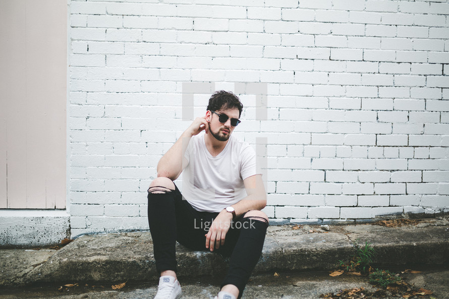 a man sitting on a curb in front of a white wall 