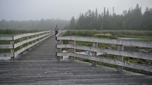 man walking over a foggy boardwalk 