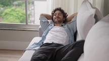 Happy, lazy young man relax daydream meditate sit on comfortable sofa at home in living room, calm guy rest breathing fresh air having nap with eyes closed feel peace of mind, no stress free relief
