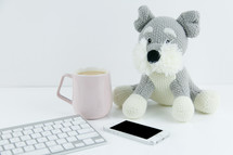 stuffed animal, computer keyboard, iPhone, and coffee mug on a desk 