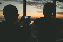 A couple taking a photo from a high rise building of the sunset.